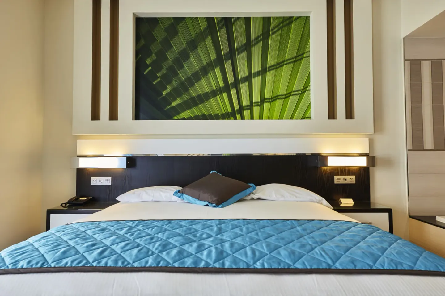 King bed with blue quilt and leaf artwork in a suite at Hotel Riu Dunamar.