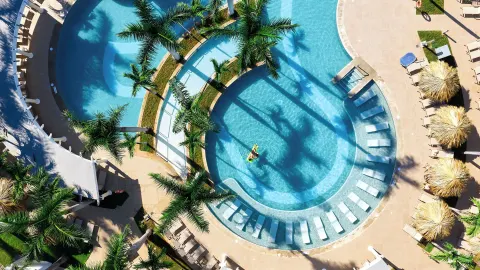 Aerial view of curved pools, palms, loungers and shaded palapas at Hotel Riu Guanacaste.