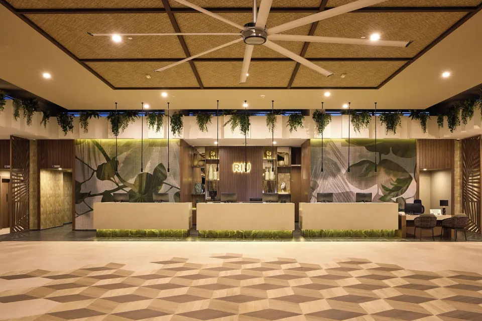 Front desk with botanical wall art and a lit RIU sign at Hotel Riu Guanacaste.