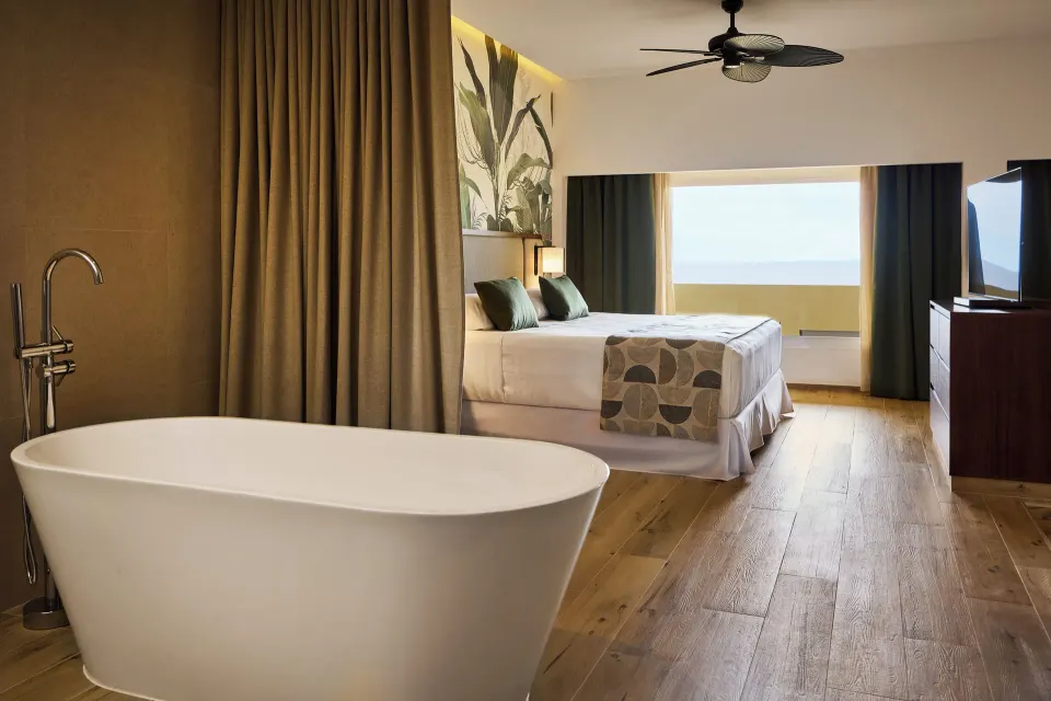 Guest room with king bed, ocean-facing window, and freestanding tub at Hotel Riu Guanacaste.