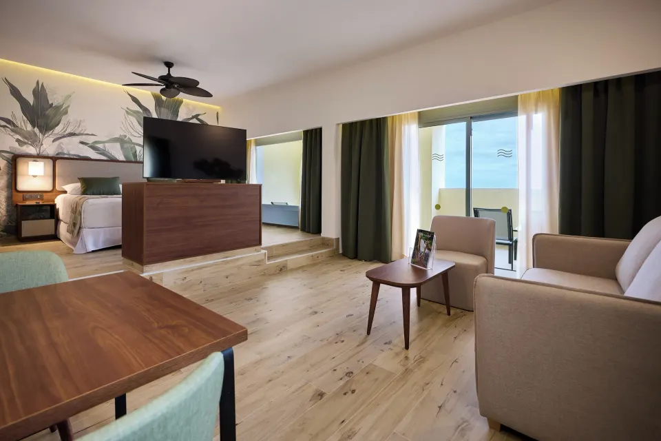 Suite living area with sofa, dining table, TV, bed alcove and balcony at Hotel Riu Guanacaste.