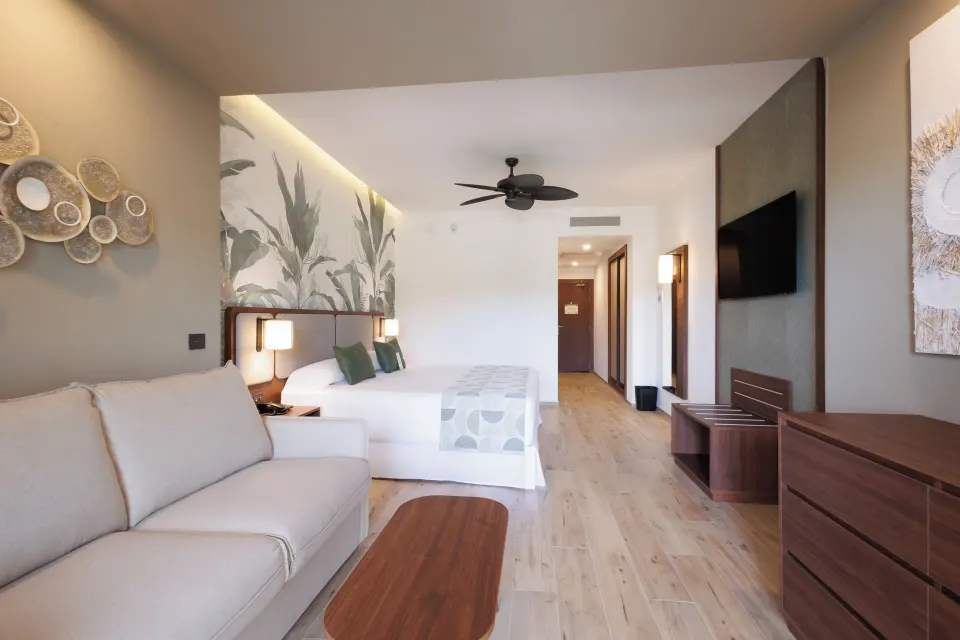 Deluxe Room Pool View with bed, sofa, TV and dresser at Hotel Riu Guanacaste.