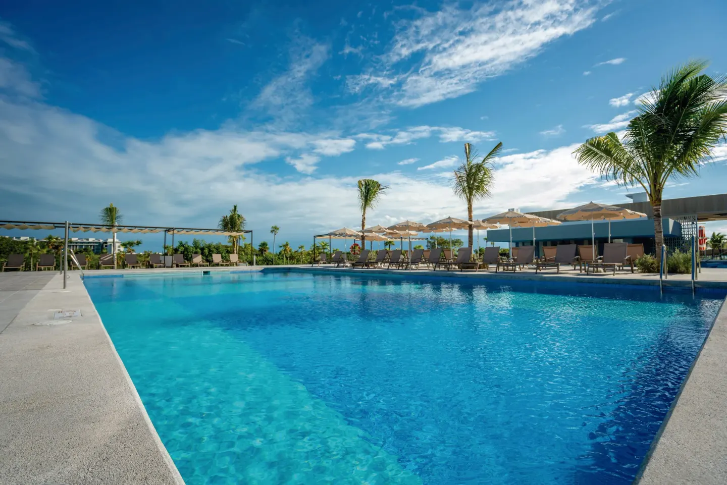Blue swimming pool with umbrellas, loungers, and palms at Hotel Riu Latino.