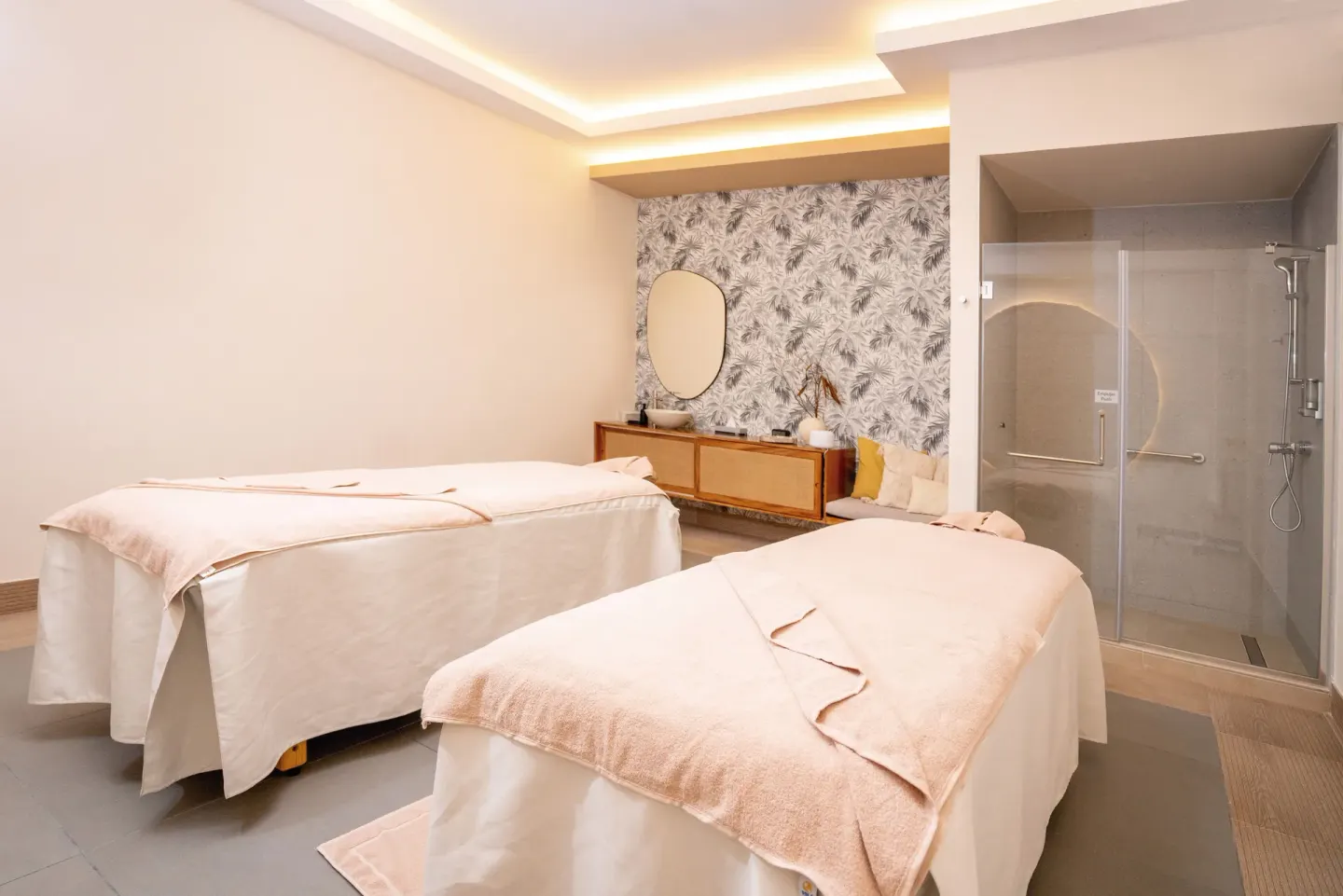 Spa treatment room with two massage tables and a glass shower at Hotel Riu Latino.