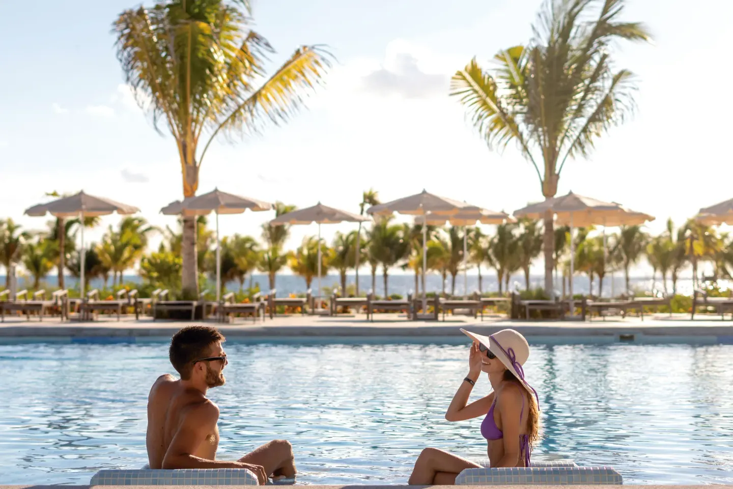 Two guests sitting in the pool with palms and umbrellas at Hotel Riu Latino.