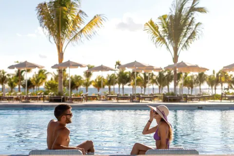 Two guests sitting in the pool with palms and umbrellas at Hotel Riu Latino.