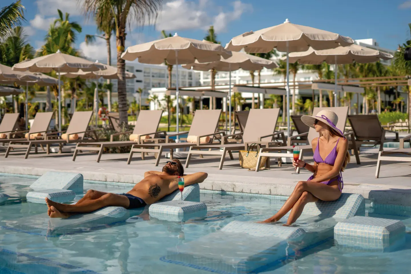 Poolside loungers, umbrellas, and guests on in-water seats at Hotel Riu Latino.
