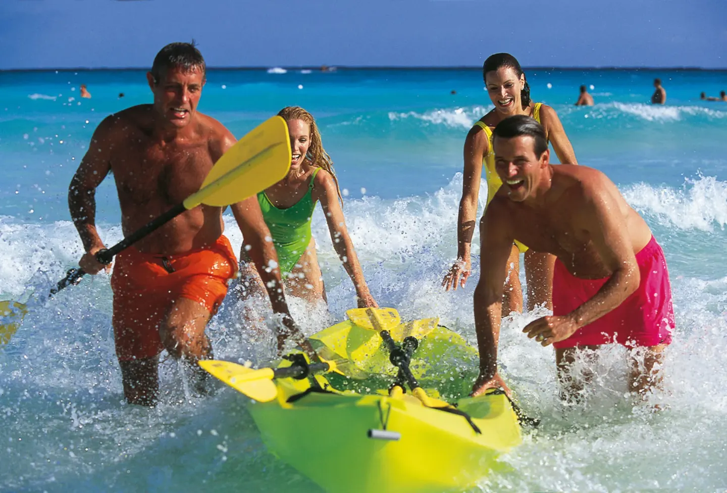 Guests run through the surf with a kayak at Hotel Riu Latino.