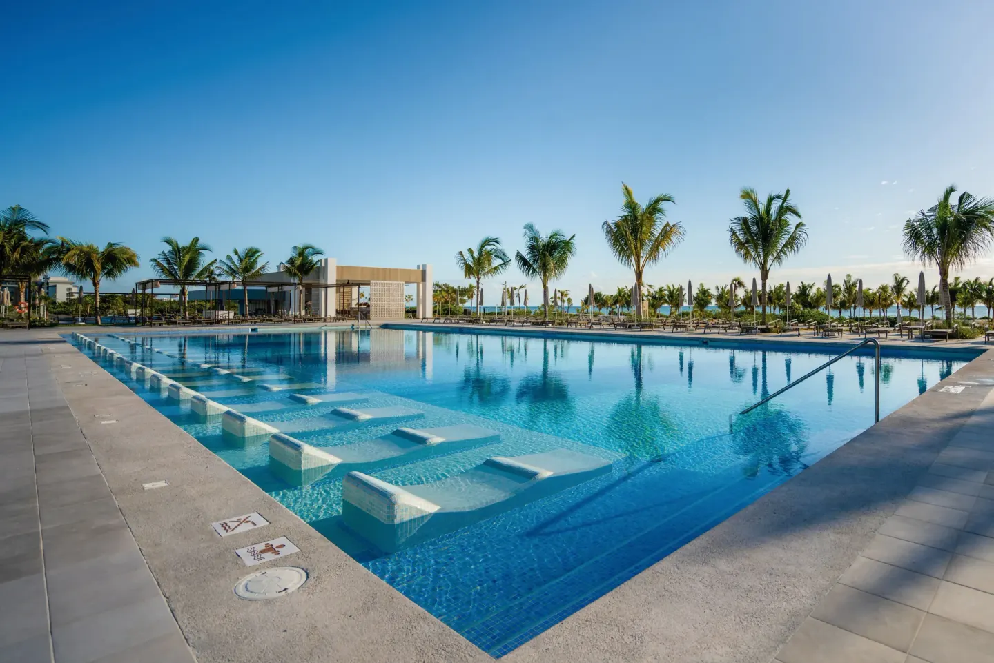 Large pool with submerged loungers and palm trees around the deck at Hotel Riu Latino.
