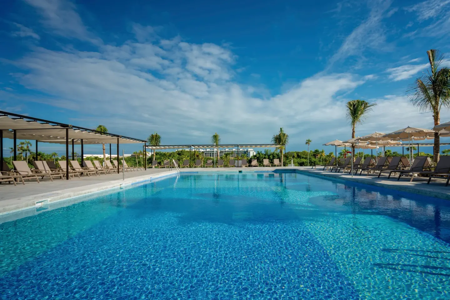 Main pool with loungers, umbrellas, and palm trees at Hotel Riu Latino.