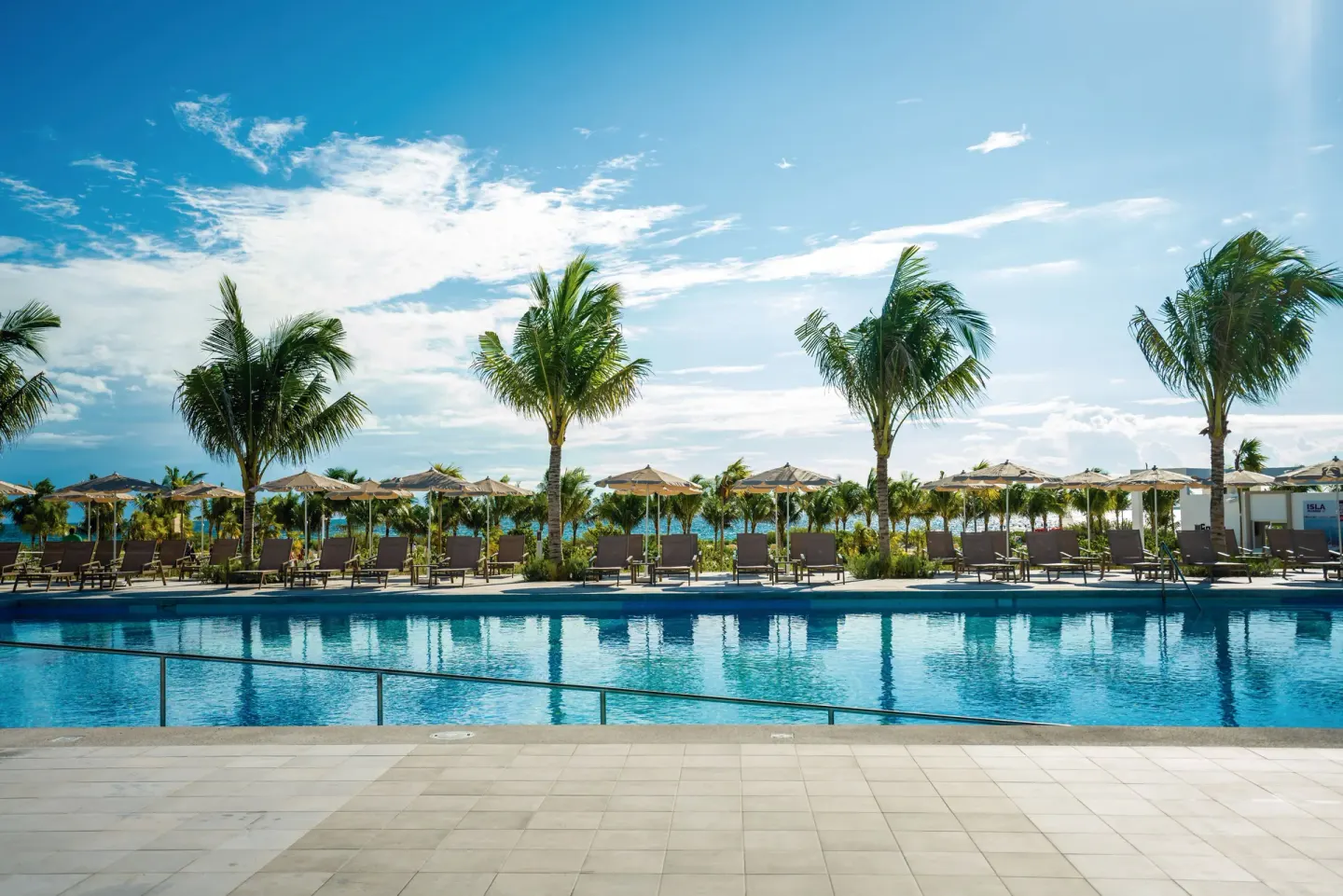 Palm-lined pool deck with sun loungers and umbrellas at Hotel Riu Latino.