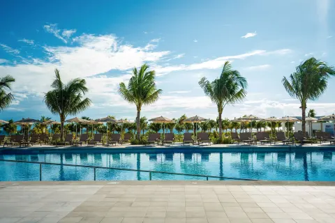 Palm-lined pool deck with sun loungers and umbrellas at Hotel Riu Latino.