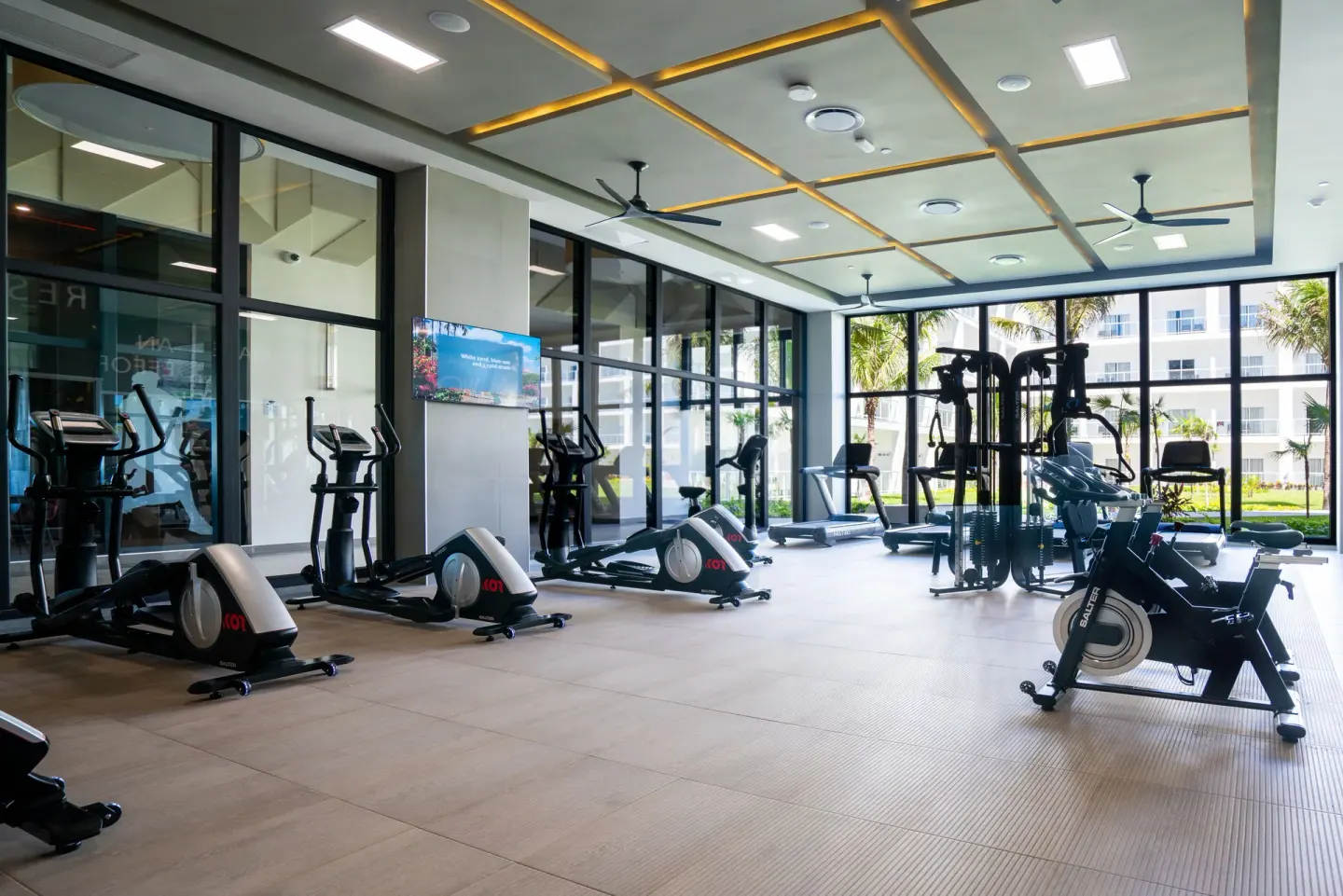 Bright gym with cardio and strength machines beside windows at Hotel Riu Latino.