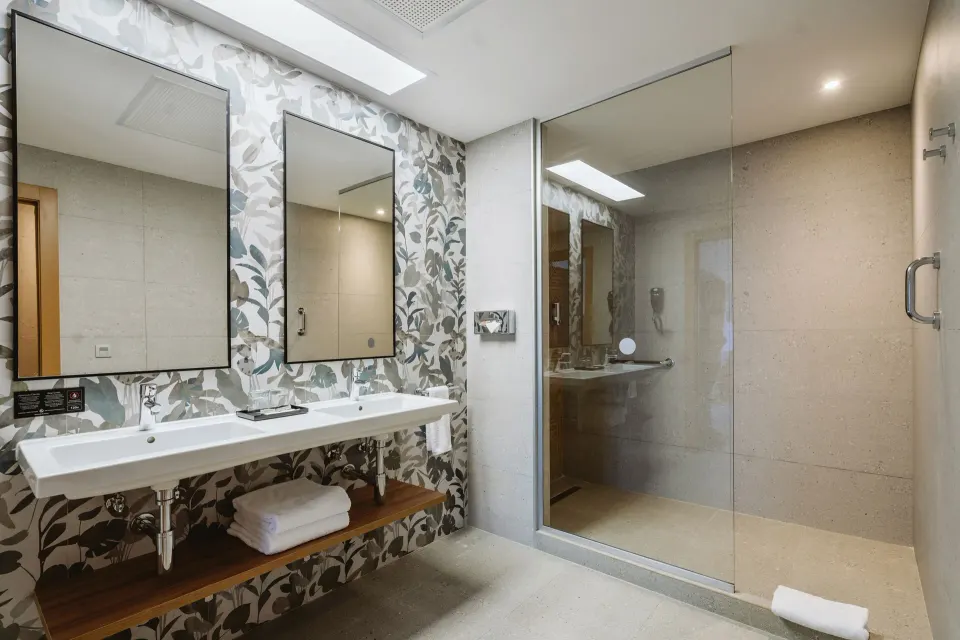 Guest room bathroom with double sinks and glass shower at Hotel Riu Latino.
