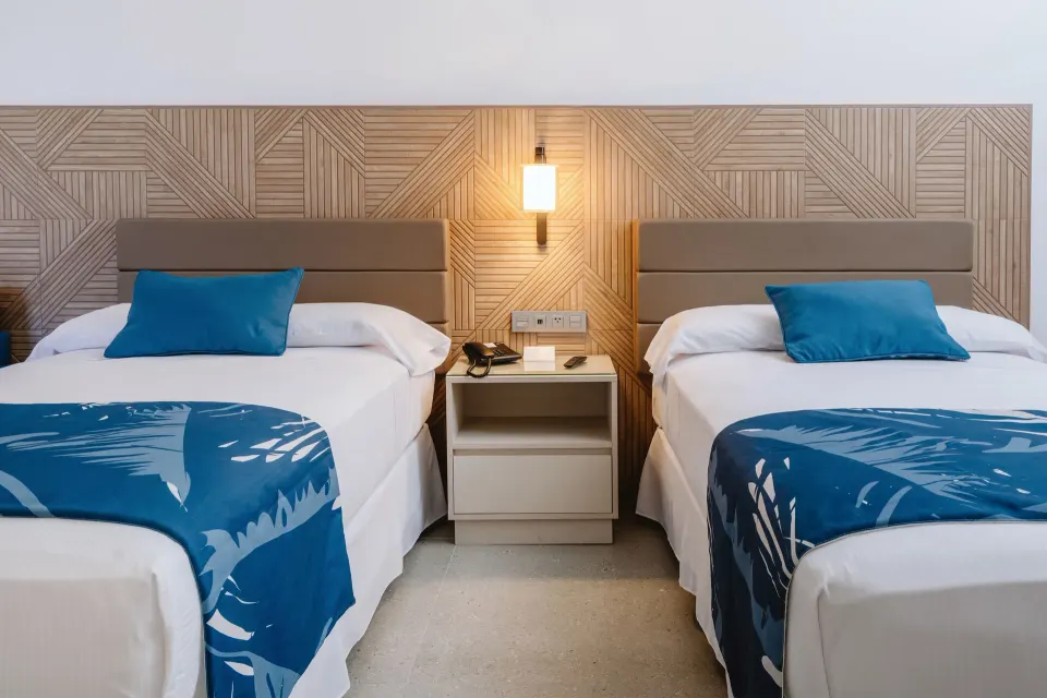 Two beds with blue accents and a shared nightstand in a guest room at Hotel Riu Latino.