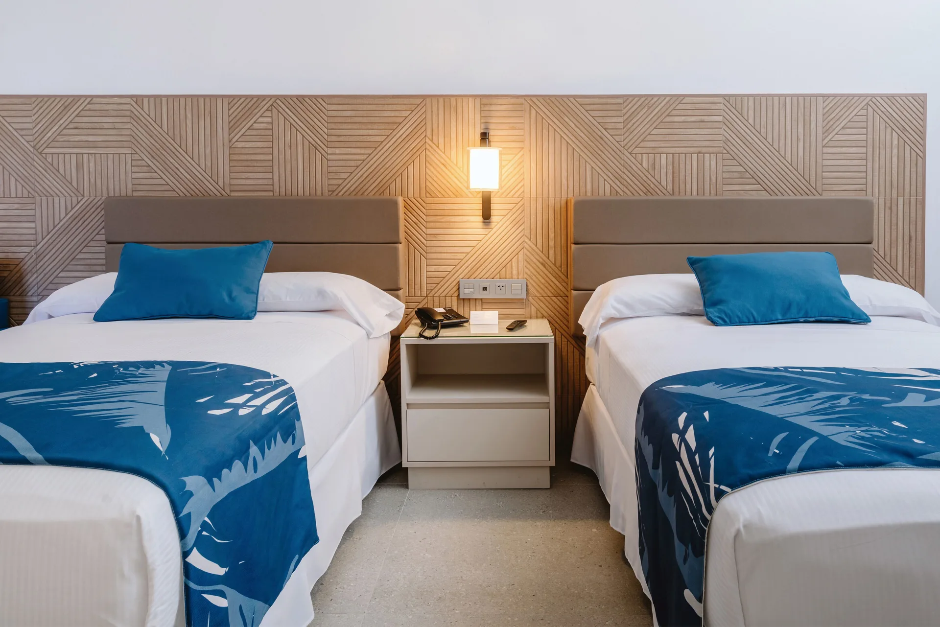 Two beds with blue accents and a shared nightstand in a guest room at Hotel Riu Latino.