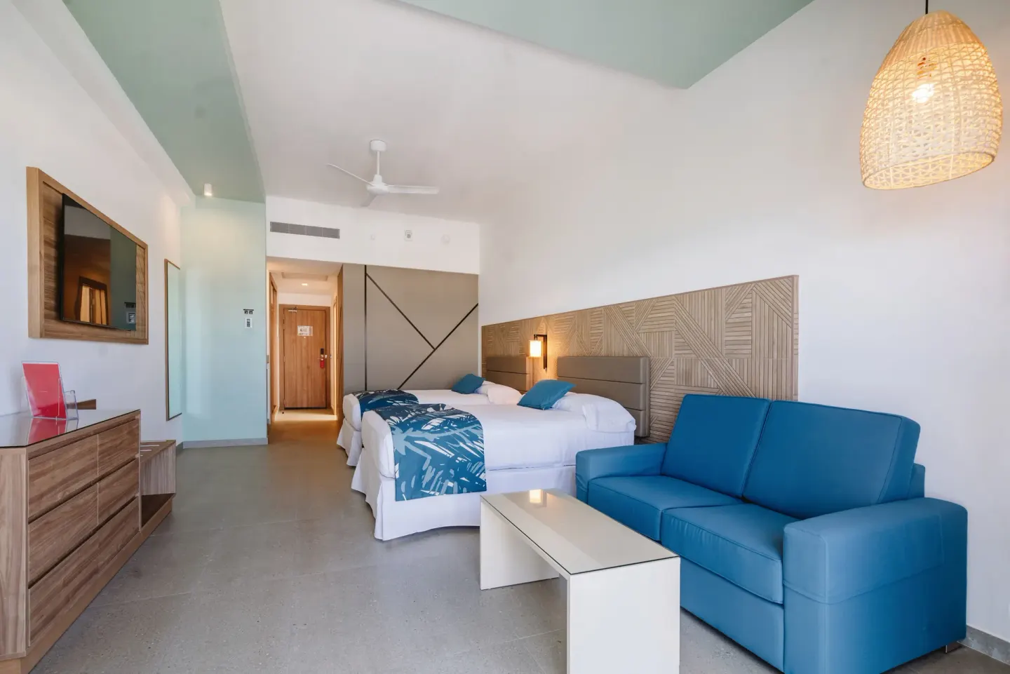 Partial Ocean View room with two beds, blue sofa, TV, and coffee table at Hotel Riu Latino.