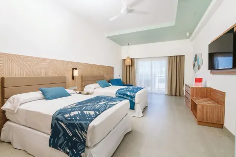 Room Partial Ocean View at Hotel Riu Latino with two beds, blue accents, balcony doors, dresser, and TV.
