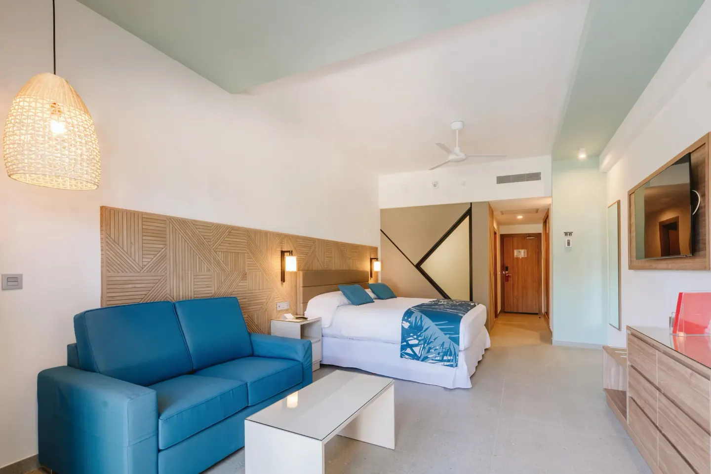 Ocean View Standard Room seating area with blue sofa and king bed at Hotel Riu Latino.