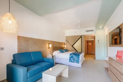 Ocean View Standard Room seating area with blue sofa and king bed at Hotel Riu Latino.