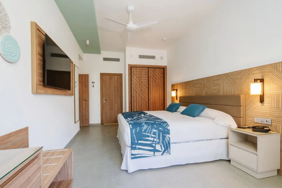 Standard Room with king bed, wall-mounted TV, and wood doors at Hotel Riu Latino.