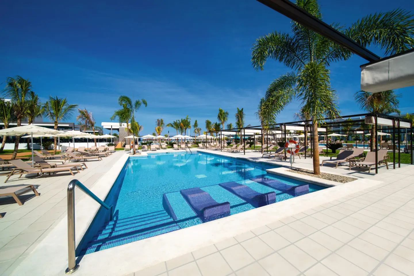 Long pool at Hotel Riu Montego Bay with submerged loungers, palms and shaded cabanas.