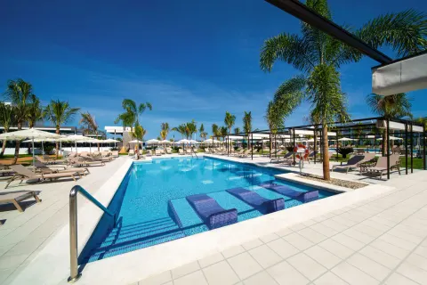 Long pool at Hotel Riu Montego Bay with submerged loungers, palms and shaded cabanas.