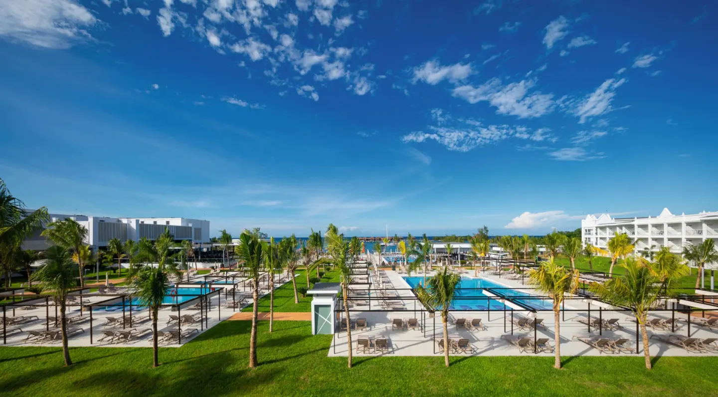 Resort grounds at Hotel Riu Montego Bay with pools, palms, lounge chairs, and white guest buildings.