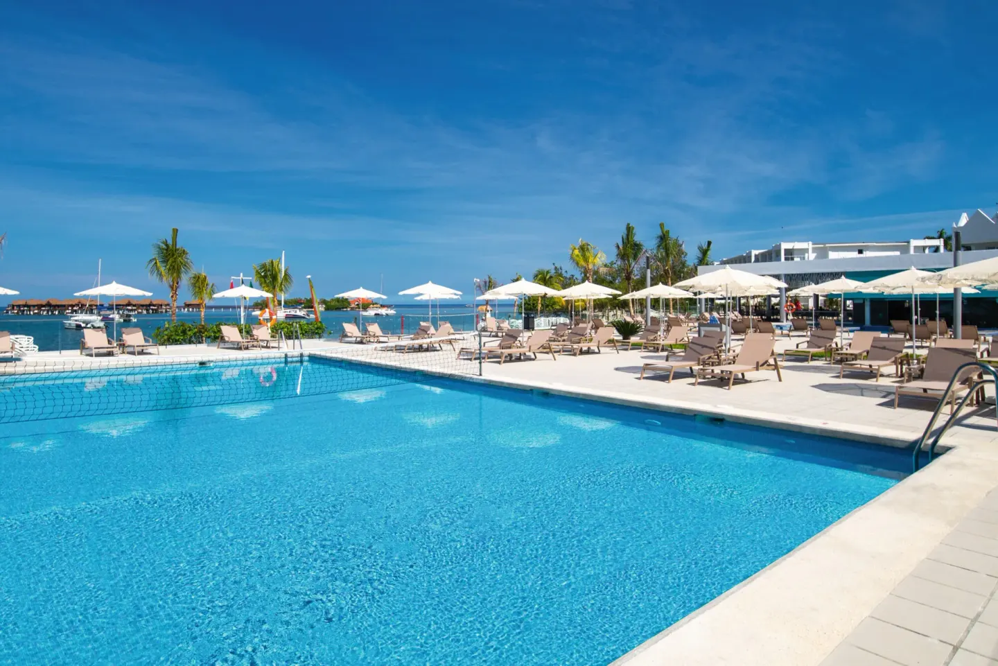 Pool deck at Hotel Riu Montego Bay with lounge chairs, umbrellas and the sea beyond.