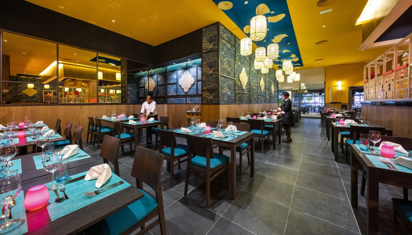 Asian-style restaurant tables with lanterns and blue accents at Hotel Riu Montego Bay.