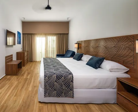 Guest room with king bed, dresser, wall-mounted TV and balcony curtains at Hotel Riu Montego Bay.