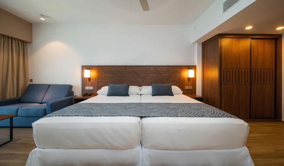 Guest room bed, blue sofa, and wood wardrobe at Hotel Riu Montego Bay.