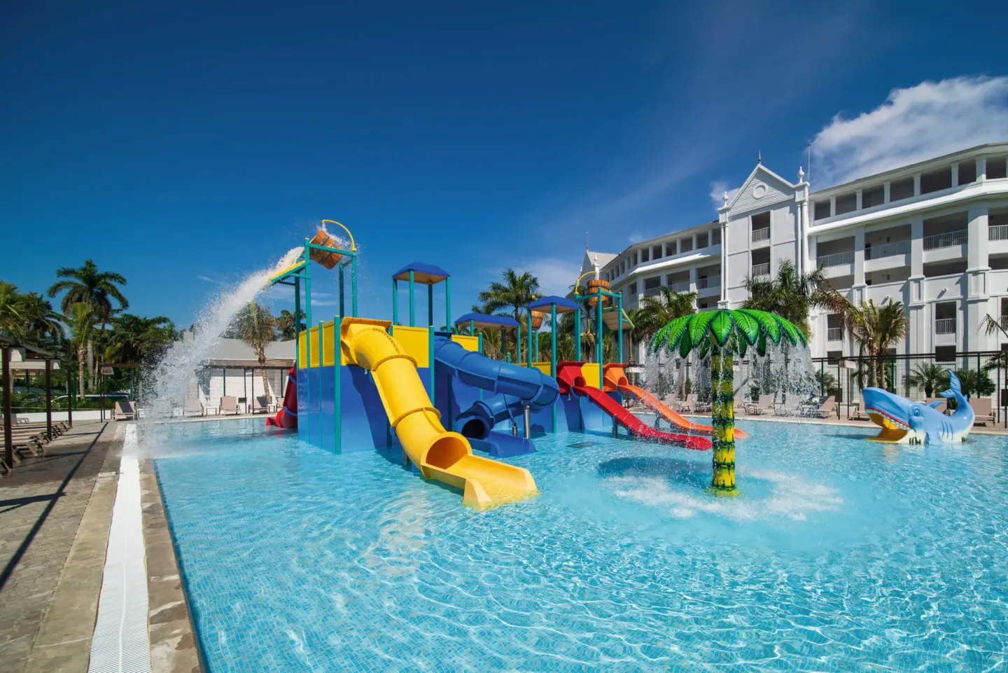 Children's pool with yellow and blue slides, a palm sprayer and shark figure at Hotel Riu Ocho Rios.