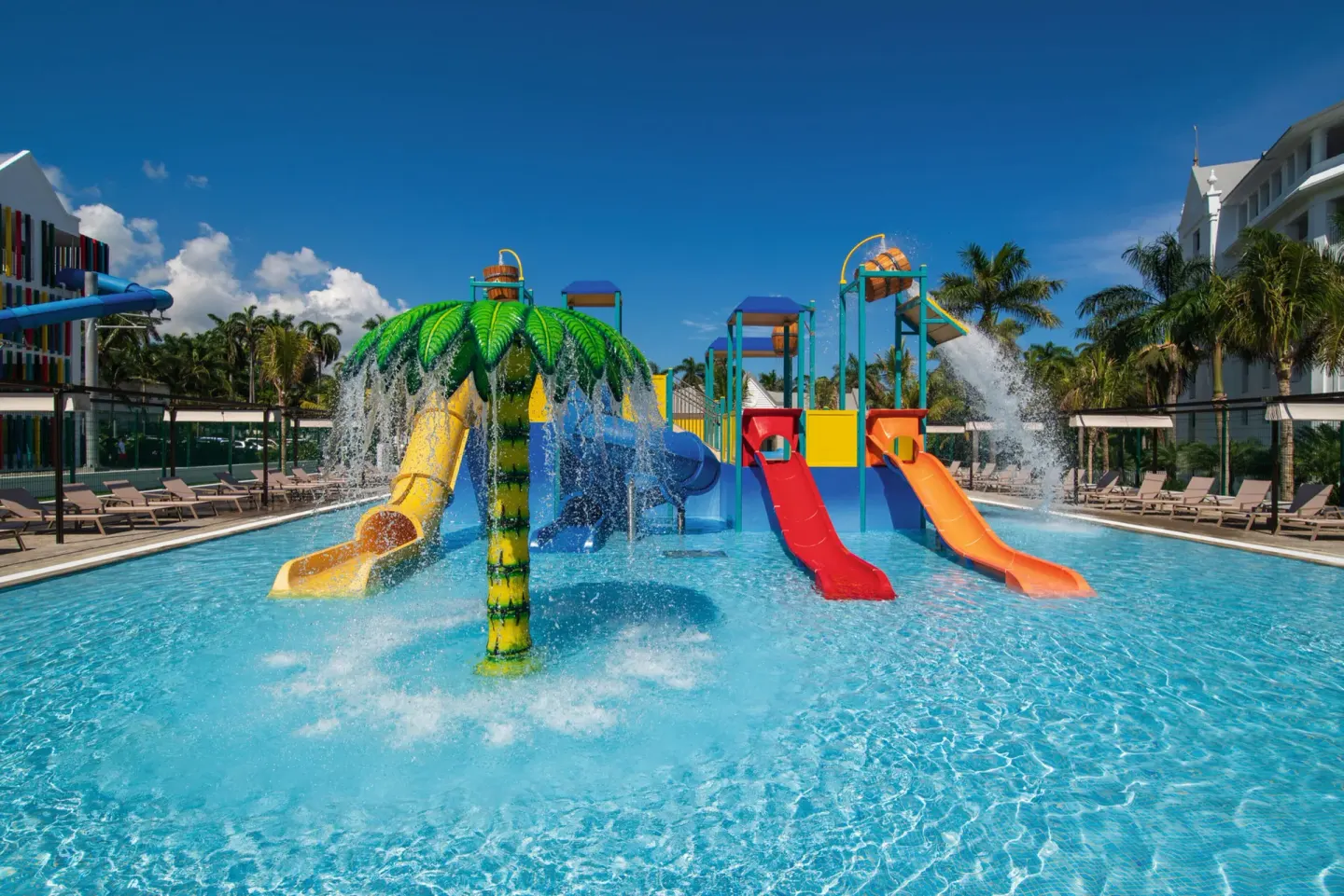 Splash pool with palm waterfall, red and orange slides, and loungers at Hotel Riu Ocho Rios.