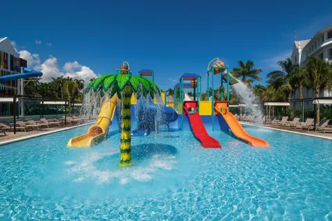 Splash pool with palm waterfall, red and orange slides, and loungers at Hotel Riu Ocho Rios.