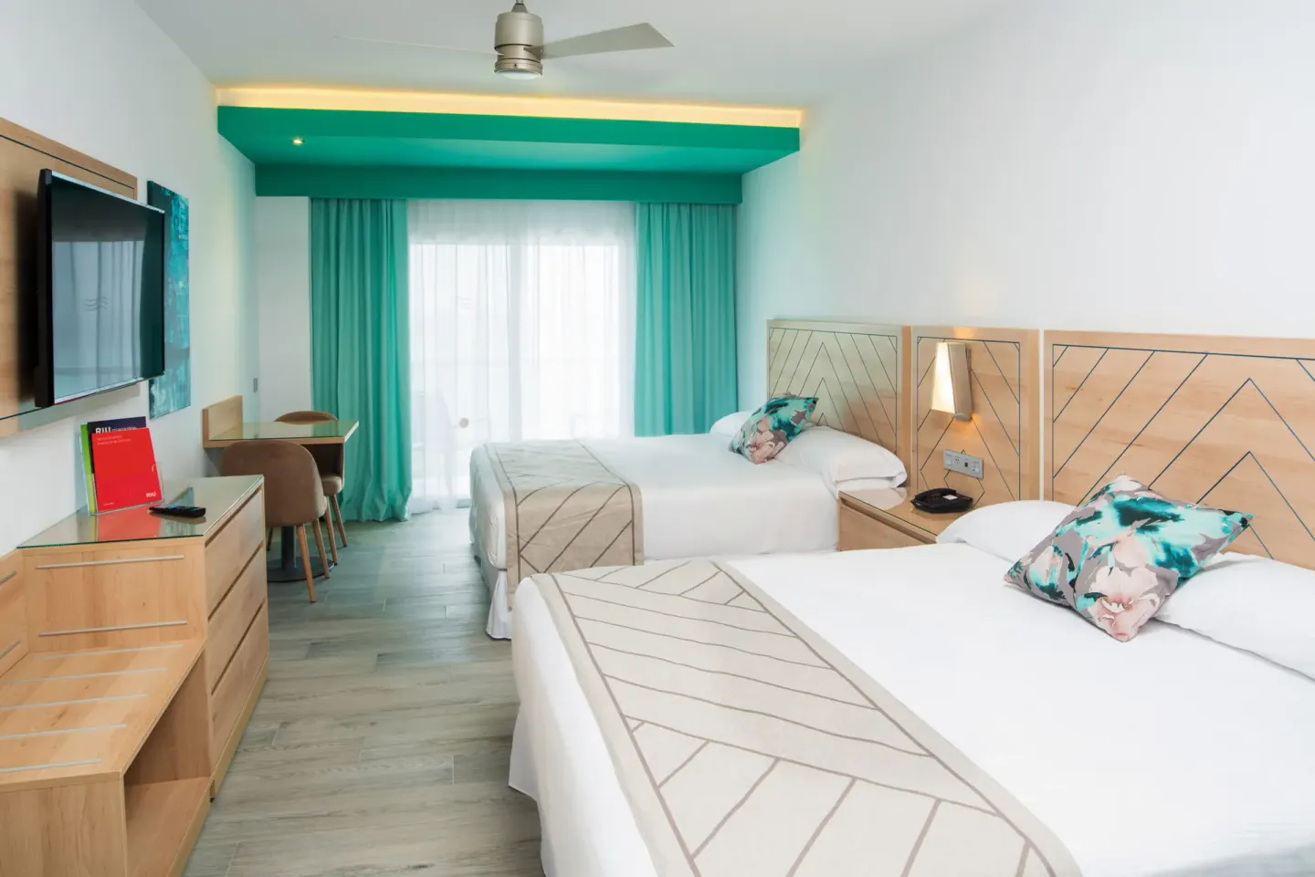 Family Room with two beds, turquoise curtains, TV, and desk at Hotel Riu Ocho Rios.