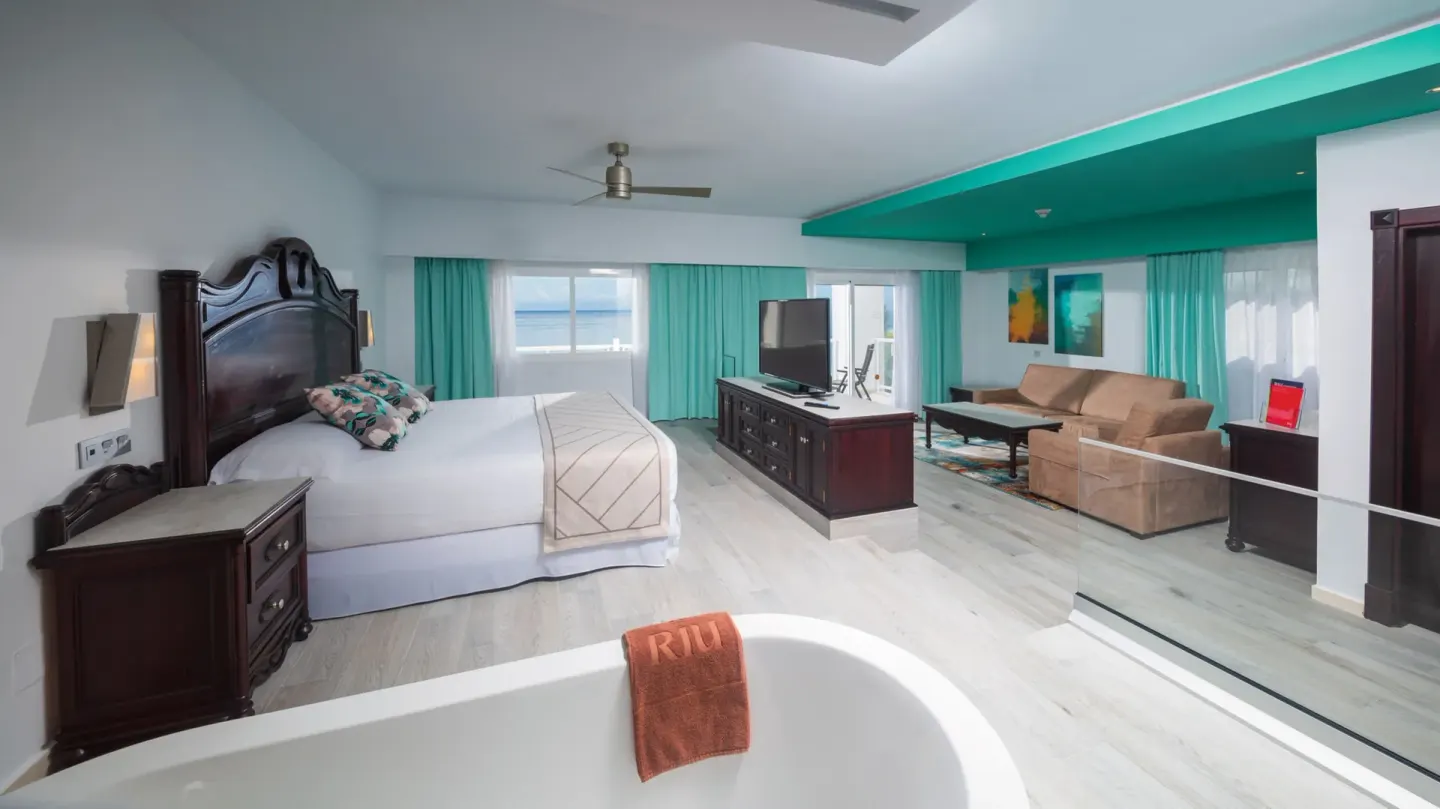 Ocean View Suite with king bed, bathtub, seating area and balcony doors at Hotel Riu Ocho Rios.