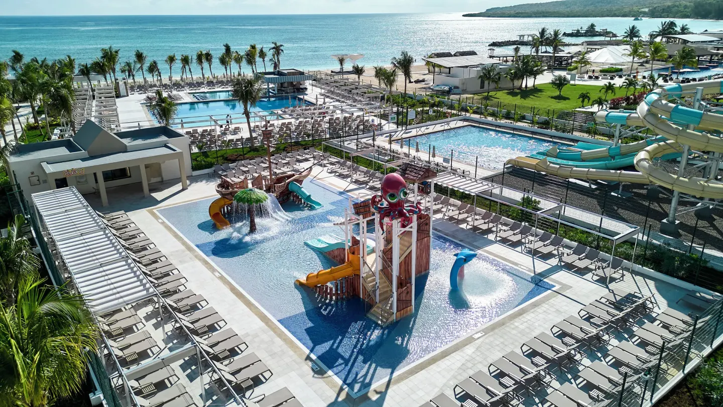 Aerial view of water park, pools, loungers, palms, and shoreline at Hotel Riu Palace Aquarelle.