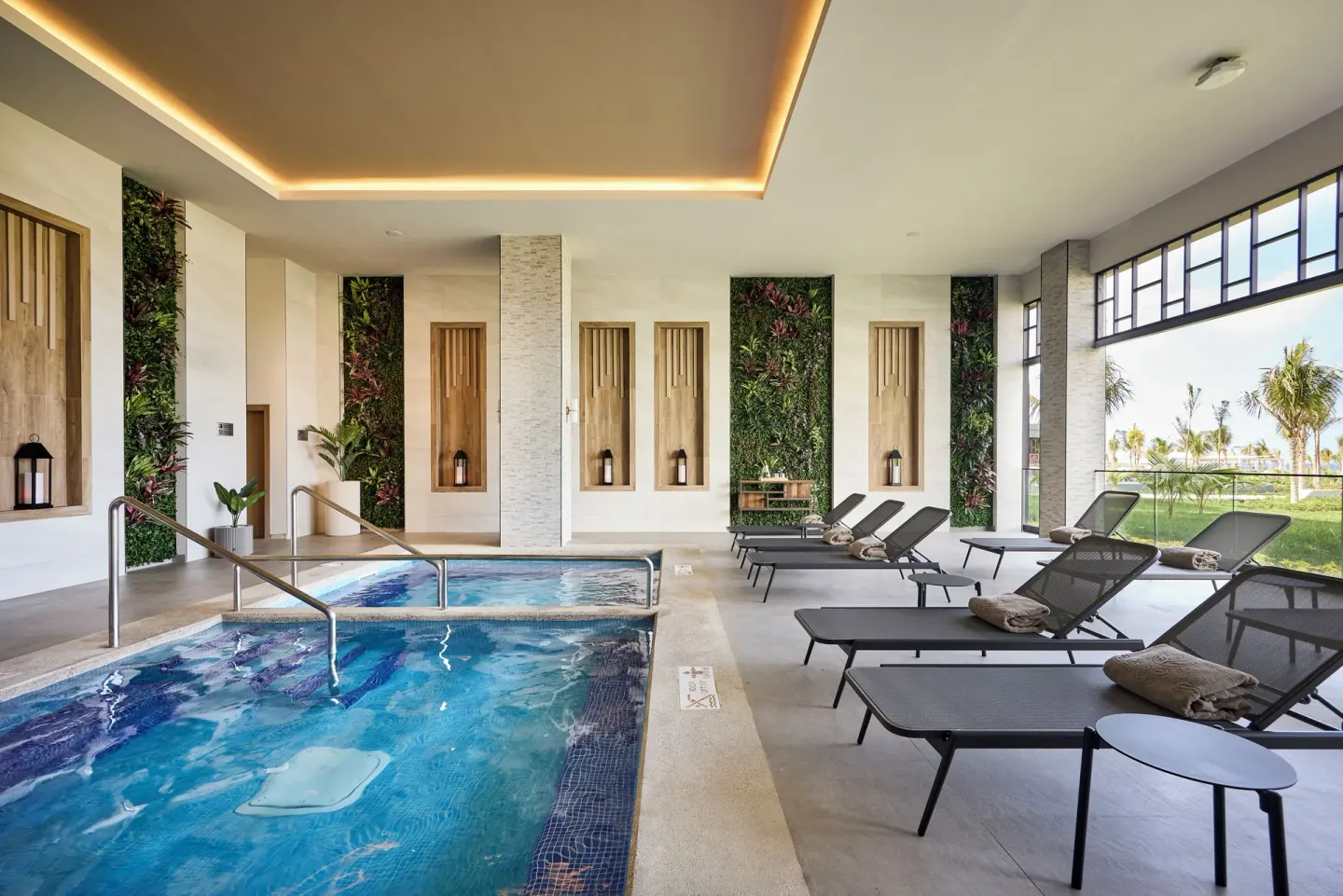 Indoor spa pool with loungers and garden-view windows at Hotel Riu Palace Aquarelle.