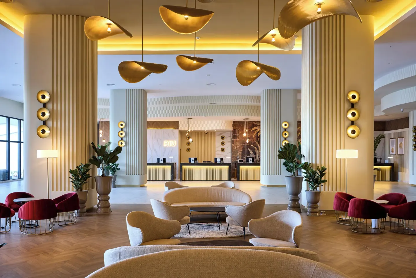 Lobby lounge at Hotel Riu Palace Aquarelle with curved seating, tall columns, and reception desks.