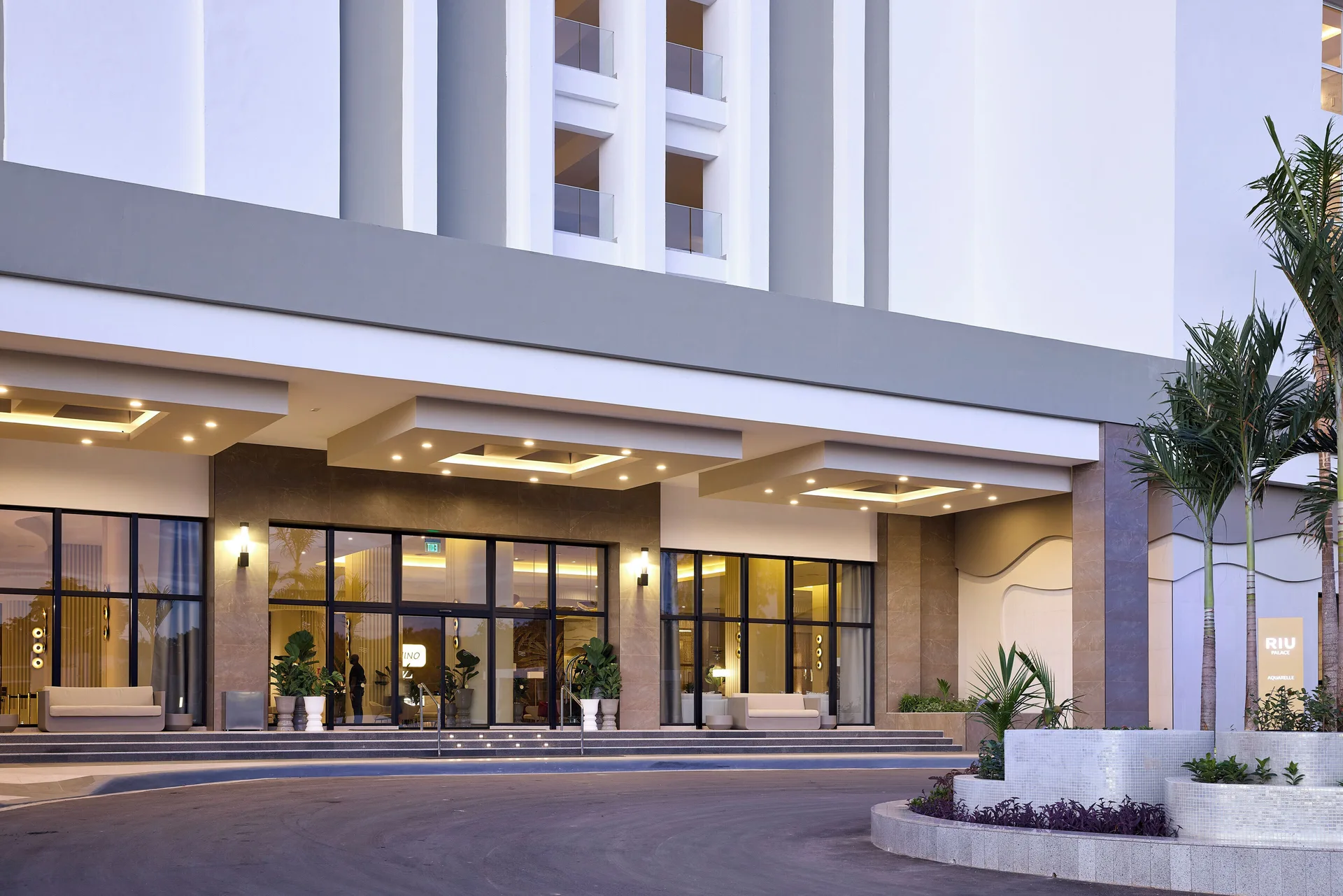 Hotel Riu Palace Aquarelle entrance with glass doors, covered drop-off, and landscaped planter.