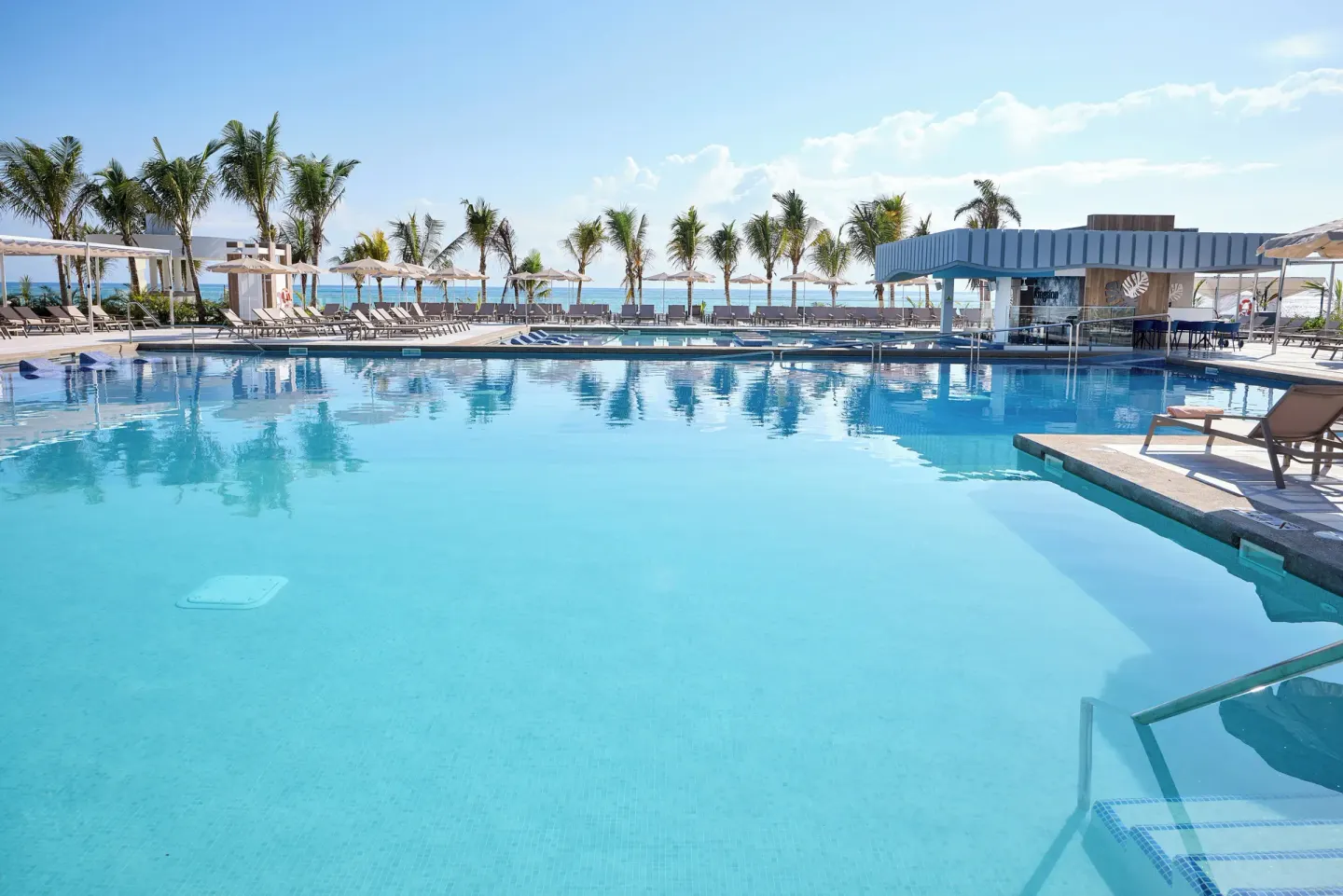 Quiet pool with loungers, palms, and a poolside bar at Hotel Riu Palace Aquarelle.