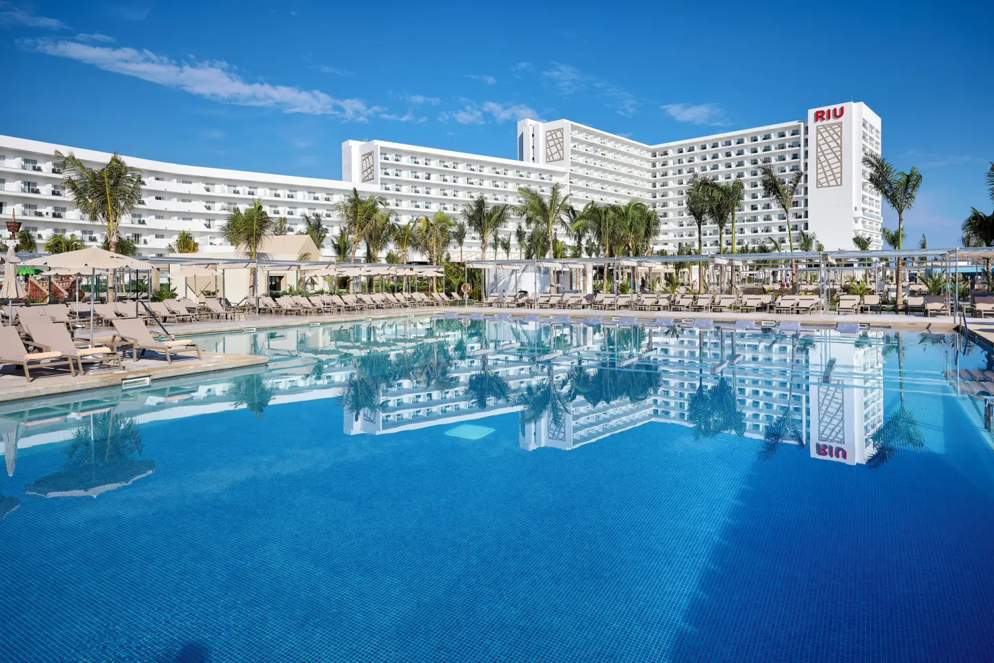 Reflective pool in front of white resort buildings at Hotel Riu Palace Aquarelle.