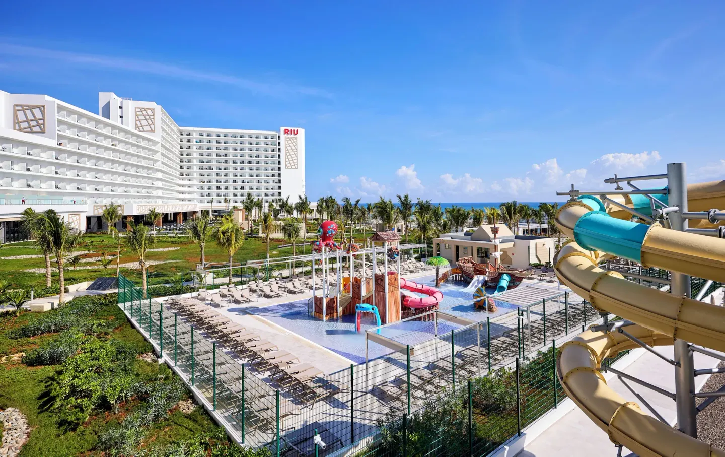 Water park with slides, splash structures, gardens, and resort buildings at Hotel Riu Palace Aquarelle.