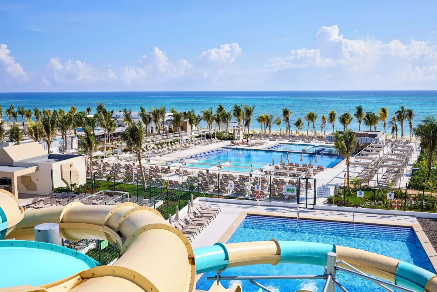Waterslide tubes overlooking pools, palm trees, and the ocean at Hotel Riu Palace Aquarelle.