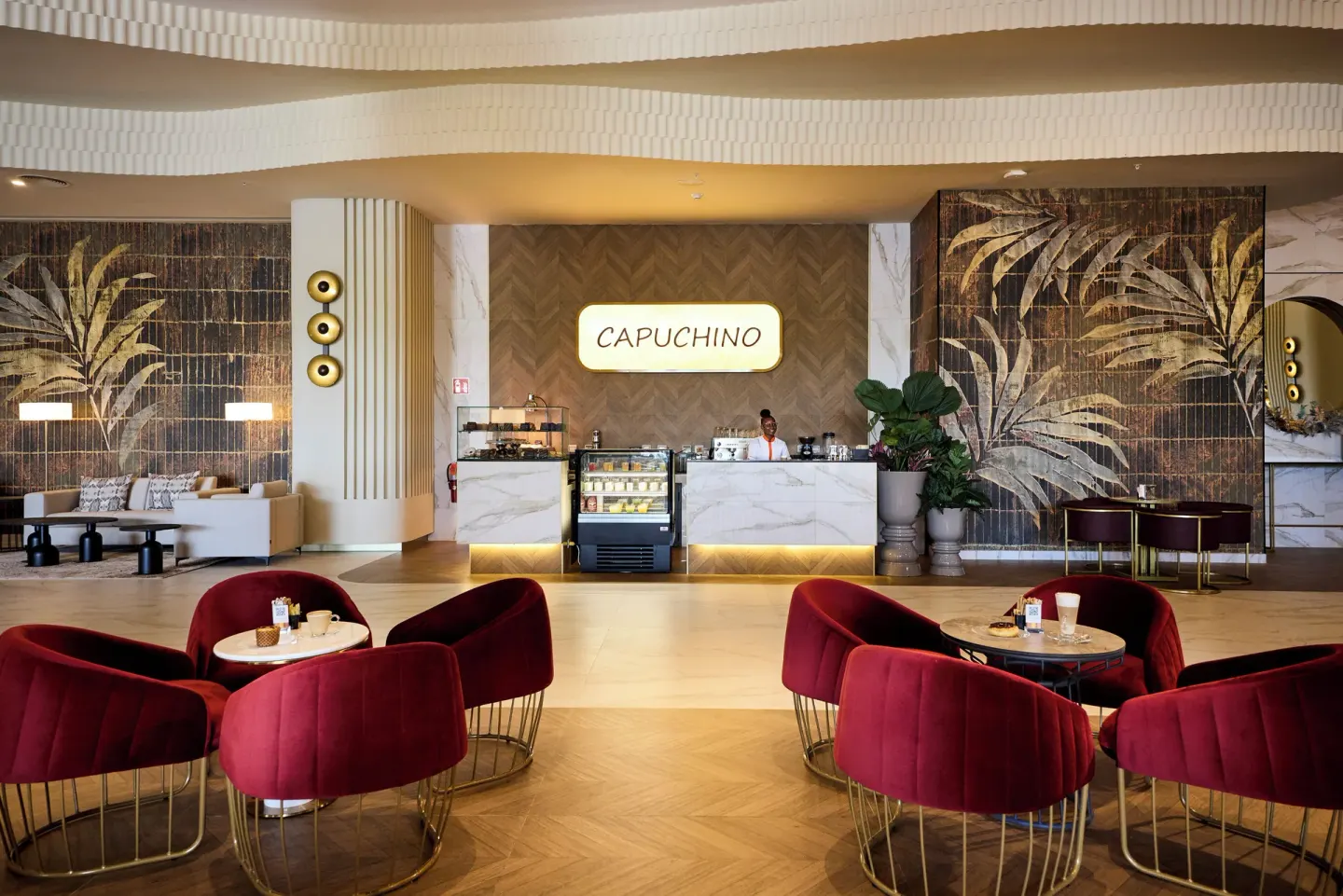Capuchino cafe lounge with red chairs and dessert counter at Hotel Riu Palace Aquarelle.