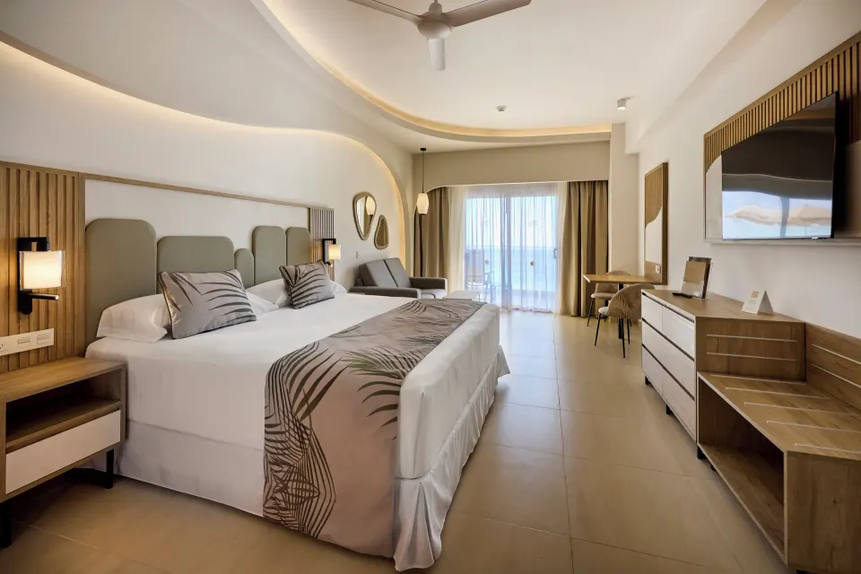 Oceanfront Junior Suite with king bed, balcony doors, and TV at Hotel Riu Palace Aquarelle.