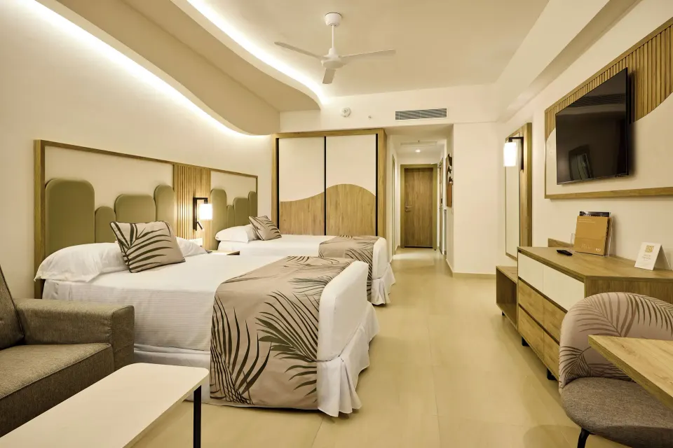 Junior Suite Partial Ocean View with two beds, sofa, TV, and desk at Hotel Riu Palace Aquarelle.