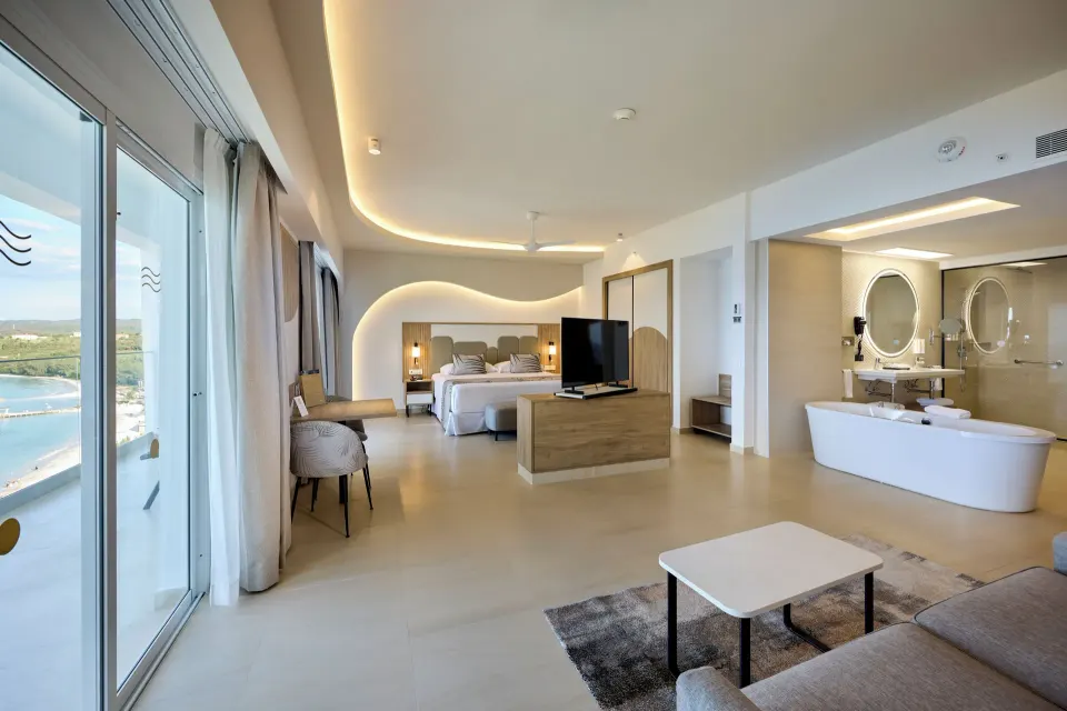 Ocean View Suite with balcony doors, bed, sofa and bathtub at Hotel Riu Palace Aquarelle.