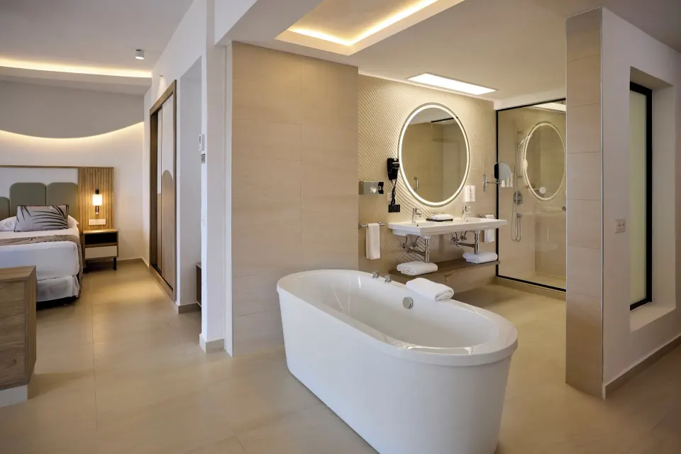 Ocean View Suite bathroom with freestanding tub and bed area at Hotel Riu Palace Aquarelle.